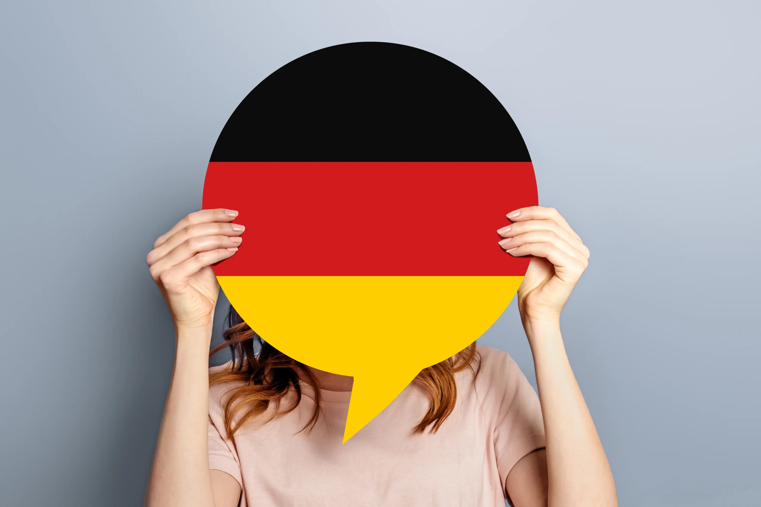 Frau hält eine Sprechblase in den Farben der deutschen Flagge vor das Gesicht, Symbolbild für den Sprachnachweis bei der Einbürgerung